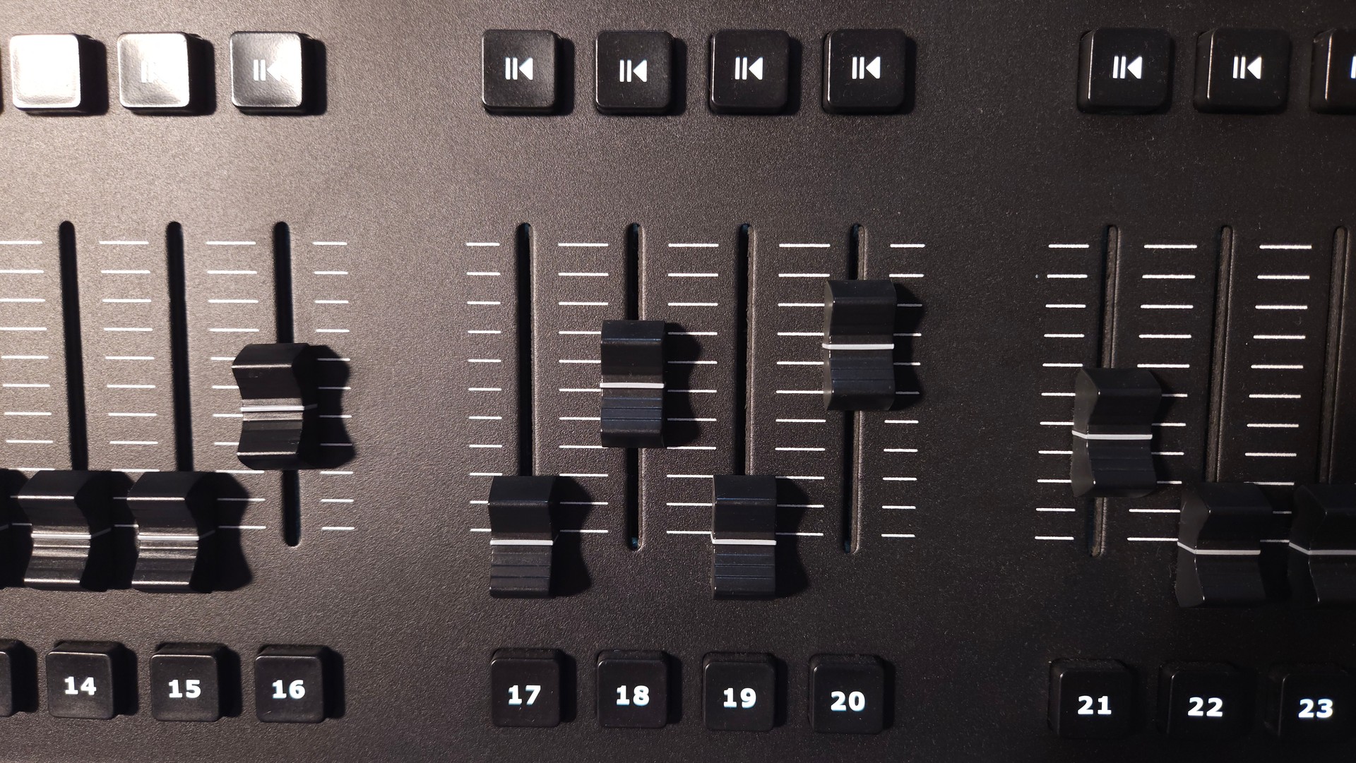 Close-up view of fader sliders and control buttons on a professional lighting control panel.